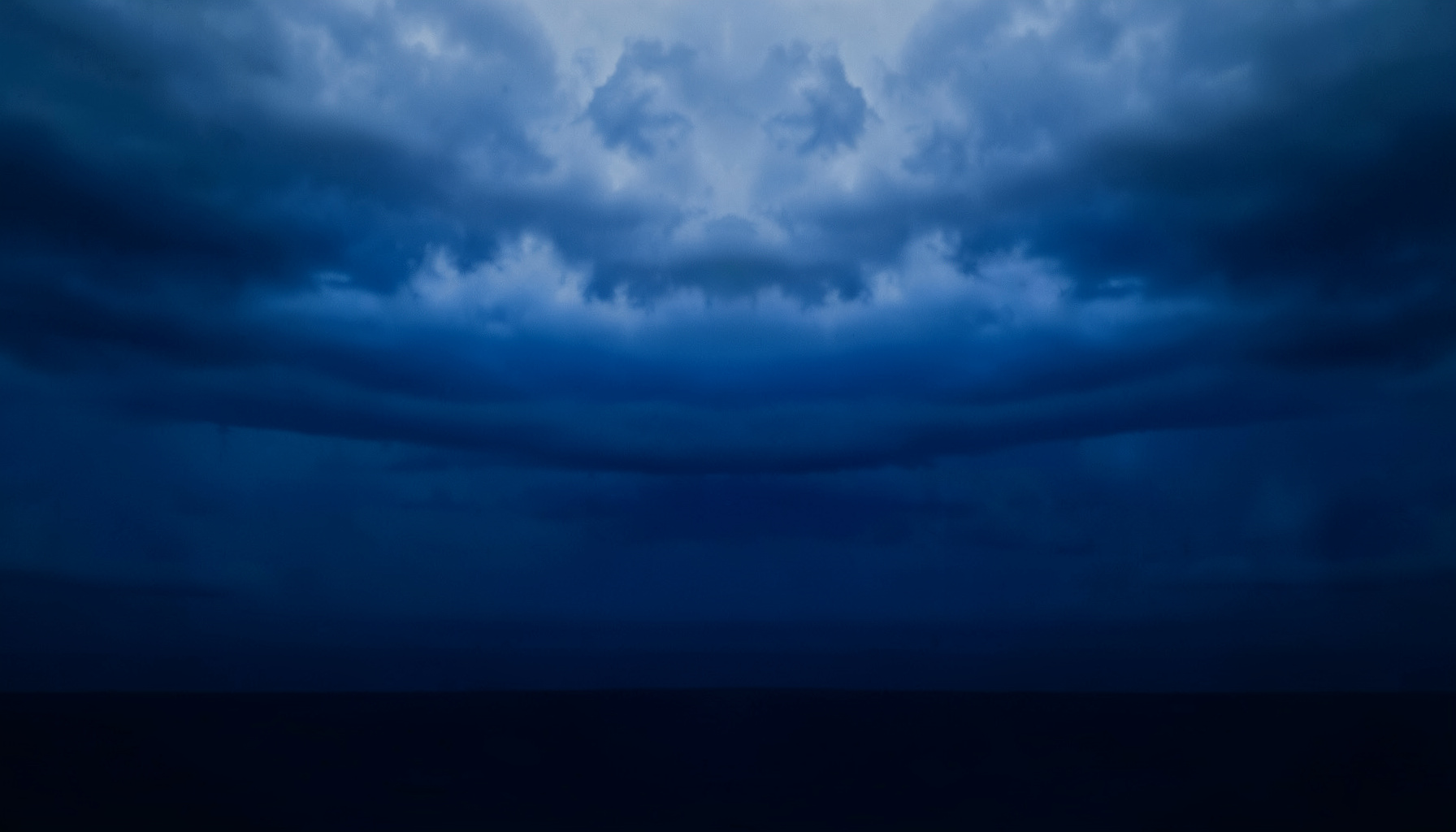 A symmetrical view of layered storm clouds over a flat horizon in deep navy blue and soft gray tones, calm and moody atmosphere
