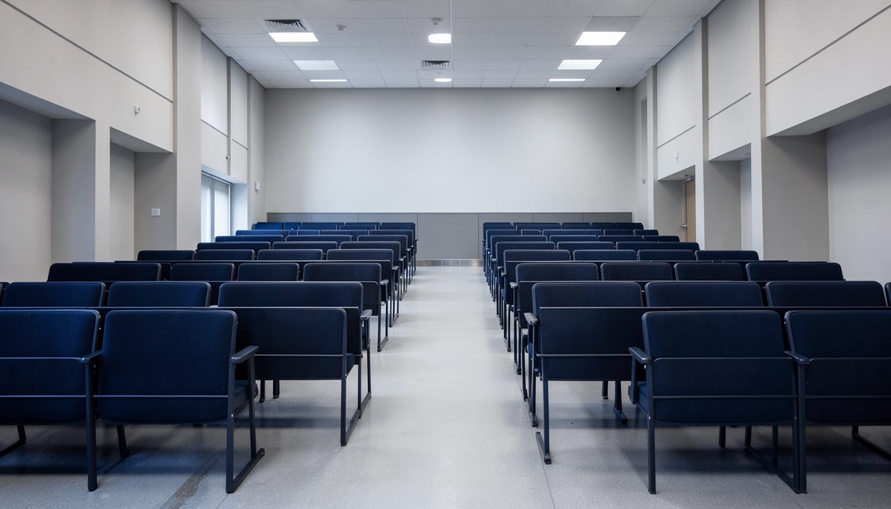 Rows of empty lecture hall seating photographed symmetrically in soft gray and navy light, calm academic mood