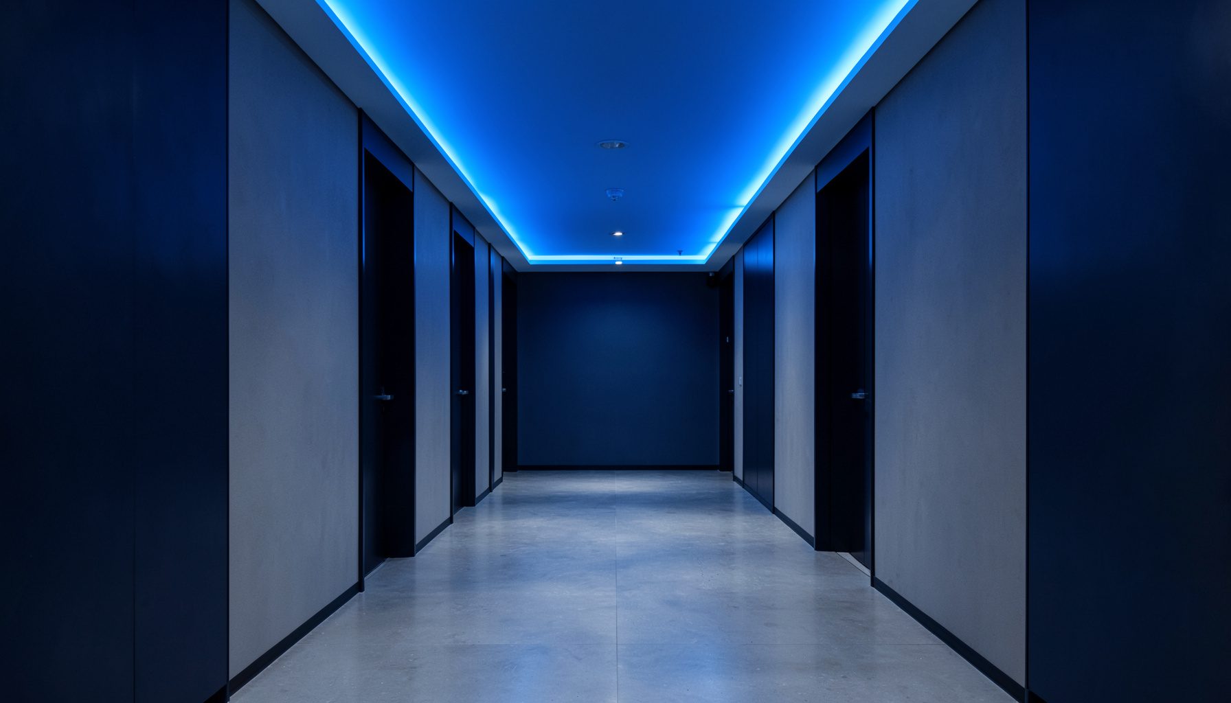 Symmetrical architectural corridor with blue overlay lighting, quiet formal mood, navy and gray palette