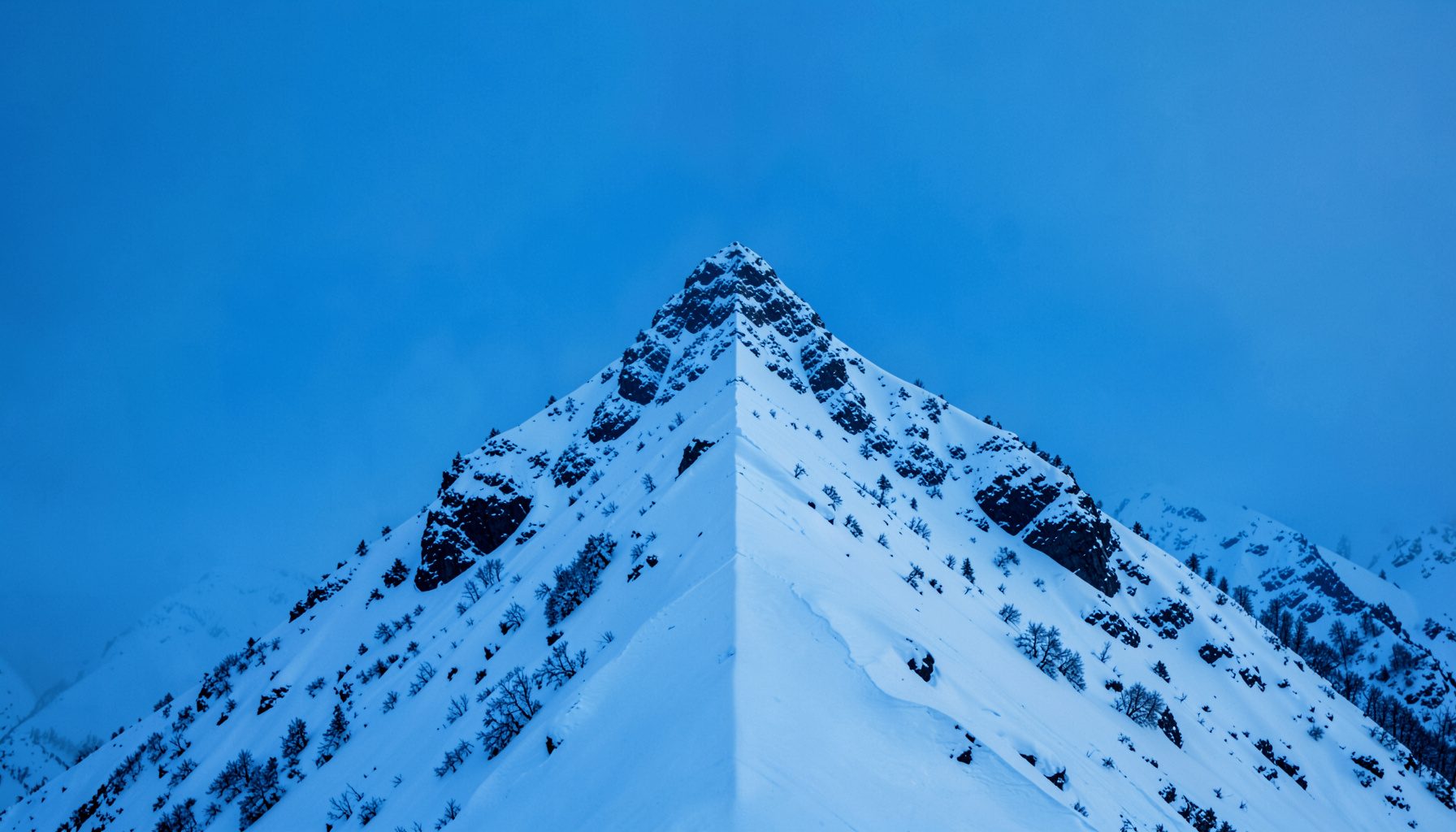 Snow-covered mountain ridge photographed with strong symmetry, cool blue and white tones, quiet and dramatic winter mood